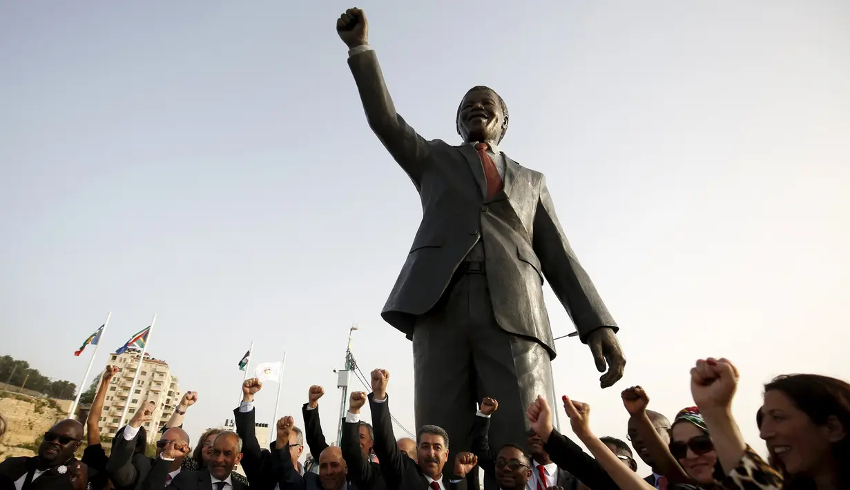 Sejumlah orang bersorak di depan patung Nelson Mandela pada peresmian di kota Ramallah, Palestina, Selasa (26/4). Patung dengan tangan kanan mengepal ke udara itu menjulang dengan ketinggian enam meter dan bobot dua ton. (REUTERS/Mohamad Torokman)