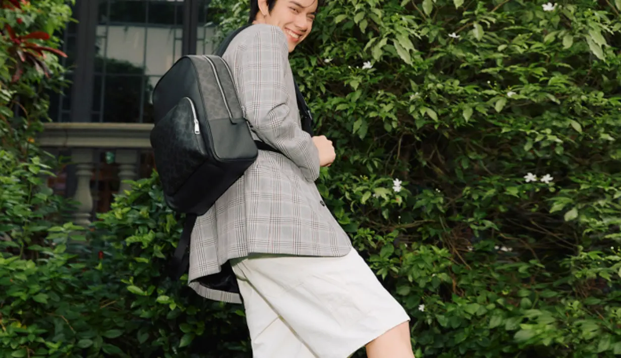 Ia tampil dengan wade backpack hitam dipadukan blazer abu-abu dipadukan celana pendek putih dan sneakers putih dan kaos kaki. [dok. Coach]