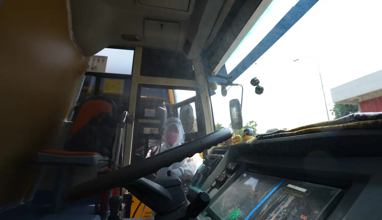 Petugas ber-APD menyemprotkan disinfektan pada bus sekolah di Posko Gabungan PSBB dan Gakplin Protkes, Puskesmas Jatinegara, Jakarta, (22/9/2020). Sejumlah unit bus sekolah kini dialihfungsikan menjadi kendaraan untuk mengantar pasien Covid-19 berstatus OTG menuju Wisma Atlet. (merdeka.com/Imam Buho