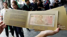 Seorang warga menunjukkan uang kertas 100 baht yang bergambar mendiang raja Thailand Bhumibol Adulyadej di Bangkok, Thailand (18/10). Uang 100 baht edisi ini dibuat untuk memperingati ulang tahun raja ke-84. (Reuters/Edgar Su)