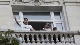 Megabintang Lionel Messi melambai kepada para fans dari balkon hotelnya di Paris, sementara sang istri Antonella Roccuzzo mengambil foto, Selasa (10/8/2021). Di Paris Saint-Germain (PSG), Messi akan dikontrak selama 2 tahun dan menerima gaji €35 juta per musim. (AP Photo/Adrienne Surprenant)
