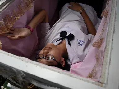 Seorang siswa remaja berbaring di dalam peti mati di Kid Mai Death Awareness Cafe, Thailand (30/3). Cafe ini menyediakan ruang pameran yang dibangun untuk mendidik masyarakat tentang kematian dan agama Buddha di Bangkok. (AFP/Lillian Suwanrumpha)