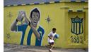 Seorang anak melewati mural bergambar Angel Di Maria menggunakan kostum Central Rosario di Santa Fe, Argentina, Minggu (5/4/2015). Central Rosario merupakan klub pertama Di Maria saat memulai karier profesional. (AFP Photo/Hector Rio)