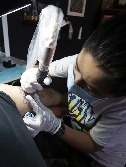 Brandon Burgos menato seseorang di kota Puebla, negara bagian Puebla, Meksiko, pada 10 November 2021. Brandon Burgos dengan hati-hati menggunakan mesin tato di studio ayahnya. Dia baru berusia 11 tahun, tetapi anak sekolah itu sudah memiliki sekitar 30 tato atas namanya. (JUAN CARLOS SANCHEZ/AFP)