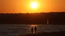 Sejumlah orang berjalan saat matahari terbenam di pantai Sampieri, Sisilia, (31/7). (AFP Photo/Ludovic Marin)