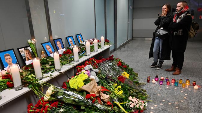 Orang-orang memandangi foto para korban pesawat 737-800 Ukraina yang jatuh di Iran, di bandara internasional Borispil, Kiev, Rabu (8/1/2020). Pesawat yang membawa 176 orang itu jatuh setelah lepas landas dari bandara utama Teheran dan menewaskan semua penumpang. (Sergei SUPINSKY/AFP)