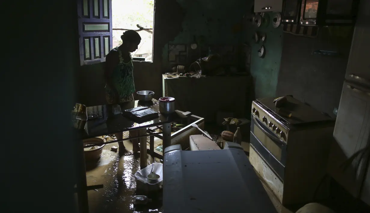 Seorang wanita membersihkan rumahnya yang terendam banjir di Itapetinga, negara bagian Bahia, Brasil, Selasa (28/12/2021). Banjir menyebabkan ribuan orang terpaksa mengungsi dari rumah mereka . (AP/Raphael Muller)