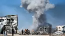 Orang-orang bergerak melewati bangunan yang hancur berlatar belakang kepulan asap menyusul serangan Israel di Jabalia, Jalur Gaza utara pada 25 Mei 2025. (Bashar TALEB/AFP)
