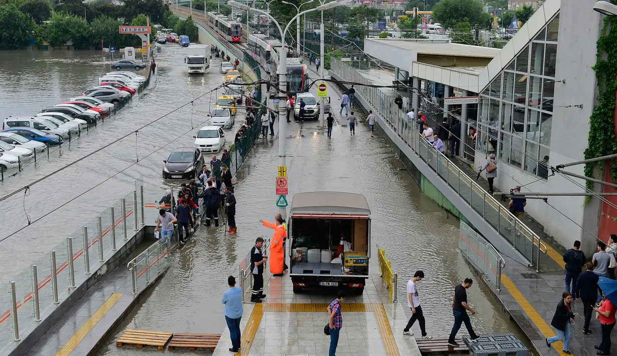 Warga berjalan di atas papan kayu melintasi banjir di stasiun metro Zeytinburnu, Selasa (18/7). Jalanan Istanbul berubah menjadi sungai akibat curah hujan yang biasanya mengguyur Turki selama satu tahun penuh, terjadi hanya dalam 12 jam. (YASIN AKGUL/AFP)