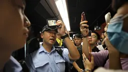 Seorang perwira polisi menunjukkan kartu anggotanya setelah pemrotes memintanya di sebuah stasiun kereta bawah tanah di Hong Kong (30/7/2019). Para Pengunjuk rasa telah mengganggu layanan kereta bawah tanah pada pagi hari. (AP Photo/Vincent Yu)