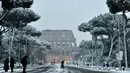 Sejumlah warga berjalan saat salju turun di dekat Colosseum di Roma, Italia (26/2). (AFP Photo/Tiziana Fabi)