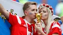 Pasangan Rusia mencium replika trofi Piala Dunia 2018 menjelang pertandingan Grup A antara Uruguay dan Rusia di Samara Arena, Samara, Rusia, Senin (25/6). (AP Photo/Rebecca Blackwell)