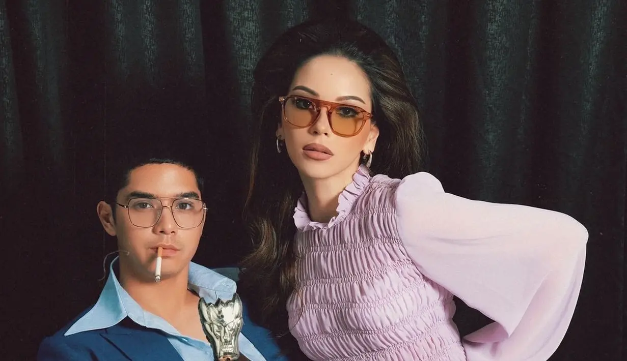 Dalam foto ini, Al Ghazali duduk di kursi dengan mengenakan setelan jas biru tua yang khas, lengkap dengan kemeja berkerah lebar yang terbuka. Dengan tatapan tajam, ia memegang tongkat yang mirip dengan gaya Elvis Presley, menambah kesan berani dan karismatik. Di sampingnya, Alyssa Daguise tampil anggun dalam balutan atasan ungu muda yang bertekstur, mengingatkan kita pada gaya Priscilla yang ikonik. (Liputan6.com/IG/@alyssadaguise)