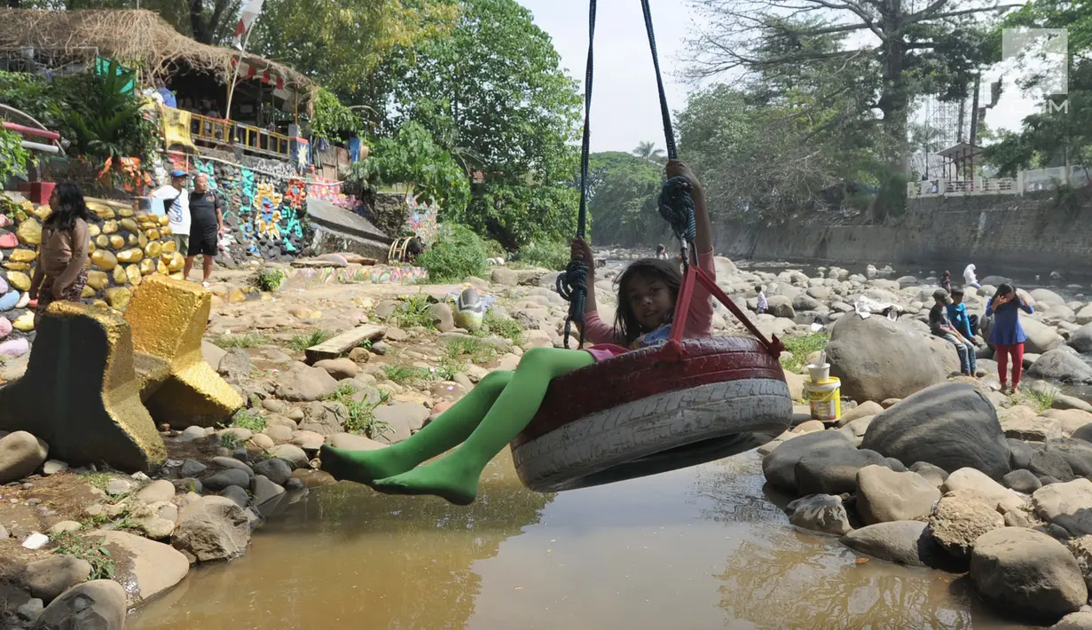 Seorang anak bermain ayunan di kolong jembatan Sempur, Bogor (16/9). Musim kemarau yang menyebabkan debit Sungai Ciliwung menyusut drastis dimanfaatkan warga Bogor dan sekitarnya untuk berwisata murah dan gratis di aliran sungai. (Merdeka.com/Arie Basuki)