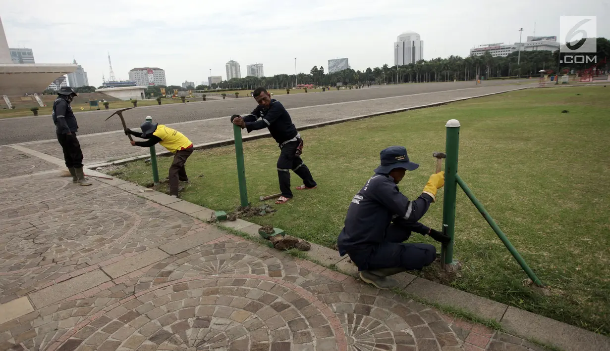Petugas Unit Pengelola Kawasan (UPK) Monas mencopot pagar pembatas antara jalan dengan taman di kawasan Monas, Jakarta, Jumat (11/1). Ketiadaan pagar ini membuat warga yang datang bebas duduk dan berjalan di rerumputan. (Liputan6.com/Arya Manggala)