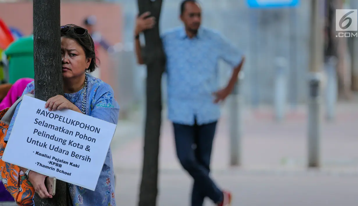Ekspresi wanita yang memeluk pohon saat menggelar aksi #ayopelukpohonini di Jalan Sudirman, Jakarta, Jumat (22/9). Mereka menolak rencana Pemprov DKI Jakarta memindahkan pohon sepanjang jalan tersebut untuk pelebaran trotoar. (Liputan6.com/Faizal Fanani)