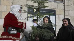 Issa Kassissieh, berpakaian seperti Sinterklas memberikan pohon Natal kepada para biarawati menjelang liburan Natal mendatang, di Kota Tua Yerusalem, Kamis (23/12/2021). Dari atas unta, dia mencoba memberikan keceriaan liburan dengan menawarkan pohon Natal grati. (AP Photo/Oded Balilty)