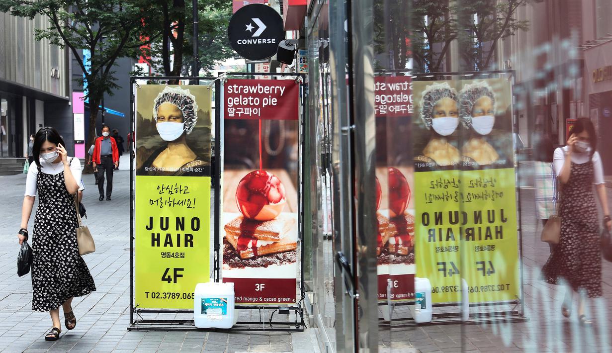Seorang wanita yang mengenakan masker untuk membantu melindungi dari penyebaran virus corona COVID-19 berjalan melewati iklan toko rambut di sebuah distrik perbelanjaan di Seoul, Korea Selatan, Kamis (2/7/2020). (AP Photo/Ahn Young-joon)