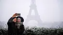 Pasangan berselfie di depan Menara Eiffel di Paris, Prancis (5/2). Ratusan orang terpaksa meninggalkan mobil mereka untuk tidur di tempat penampungan darurat akibat cuaca ekstrem yang melanda. (AFP Photo/Lionel Bonaventure)