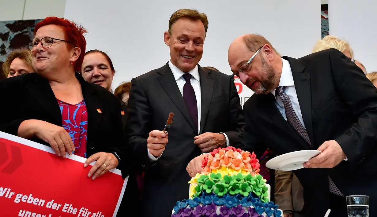 Pemimpin kelompok parlementer partai SPD, Thomas Oppermann (tengah) bersama Martin Schulz memotong kue pengantin dengan warna pelangi dan dihiasi patung-patung dua wanita dan dua pria di Bundestag di Berlin (30/6). (AFP Photo/Tobias Schwarz)