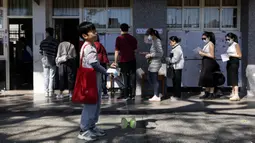 Seorang anak bermain ketika orang-orang mengantri untuk memberikan suara mereka dalam pemilihan presiden di sebuah tempat pemungutan suara di New Taipei City pada tanggal 13 Januari 2024. (Alastair PIKE/AFP)