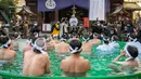 Penganut Shinto dari Kuil Teppozu Inari mandi dengan air dingin untuk mensucikan jiwa dan tubuh mereka selama ritual Tahun Baru di Tokyo, Jepang, Minggu (9/1/2022). Mereka pun satu per satu memasuki bak yang airnya dingin bahkan ada es batu di dalamnya. (Philip FONG/AFP)