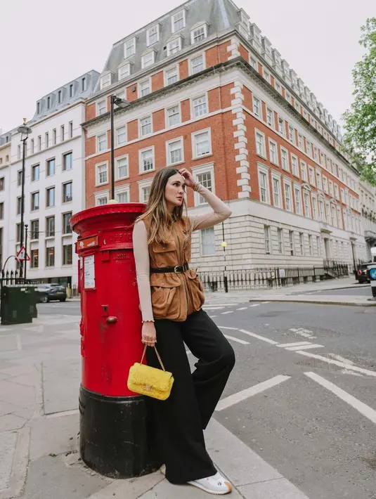 Berpose di tangga sebuah bangunan kota London, Luna Maya tampil chic memadukan sleeveless top dengan detail kantong warna caramel, dengan inner warna kulit, celana kulot hitam, dan sneakers putih. (Instagram/lunamaya).