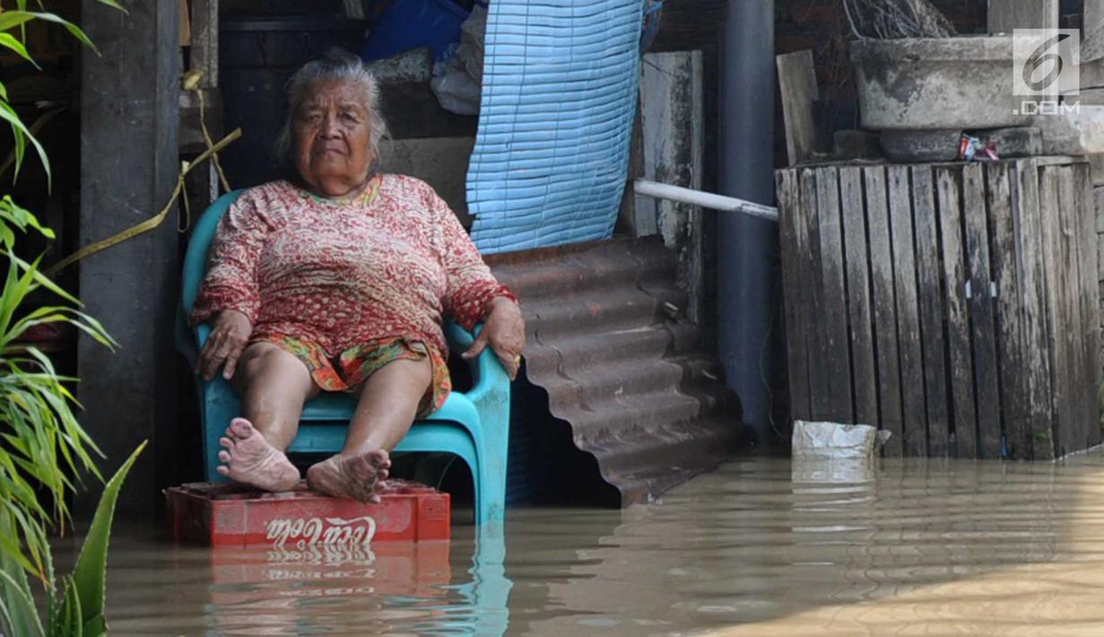 Seorang warga duduk di depan rumahnya yang tergenang banjir di kawasan Sawah besar Semarang, Jawa Tengah, Sabtu (8/12). Akibat banjir tersebut Warga pun menyelamatkan diri tanpa sempat membawa barang pribadi miliknya. (Liputan6.com/Gholib)