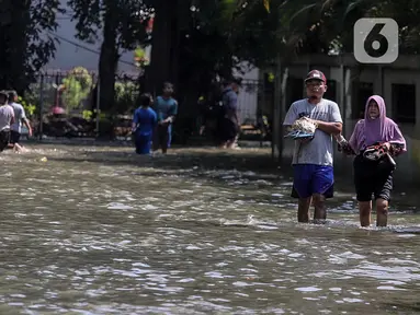 Warga melintasi genangan air yang merendam jalan di kawasan Kampung Makasar, Jakarta Timur, Senin (7/7/2025). (Liputan6.com/Herman Zakharia)