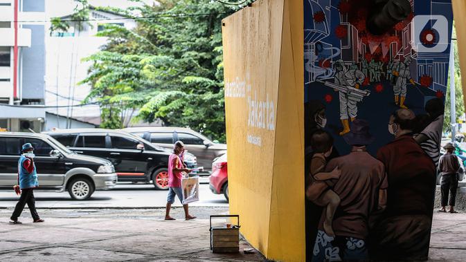 Sejumlah pedagang berjalan di dekat mural imbauan untuk melawan COVID-19 di Jakarta, Kamis (17/11/2020). Menurutnya, capaian tersebut sudah lebih baik, bahkan berada di atas rata-rata tingkat kesembuhan global. (Liputan6.com/JohanTallo)