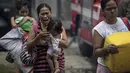 Warga membawa anak mereka mengungsi saat kebakaran melanda rumahnya di Manila, Filipina (11/8). Sejauh ini kebakaran menghancurkan 300 rumah dan mengakibatkan 800 keluarga harus dievakuasi. (AFP Photo/Noel Celis)