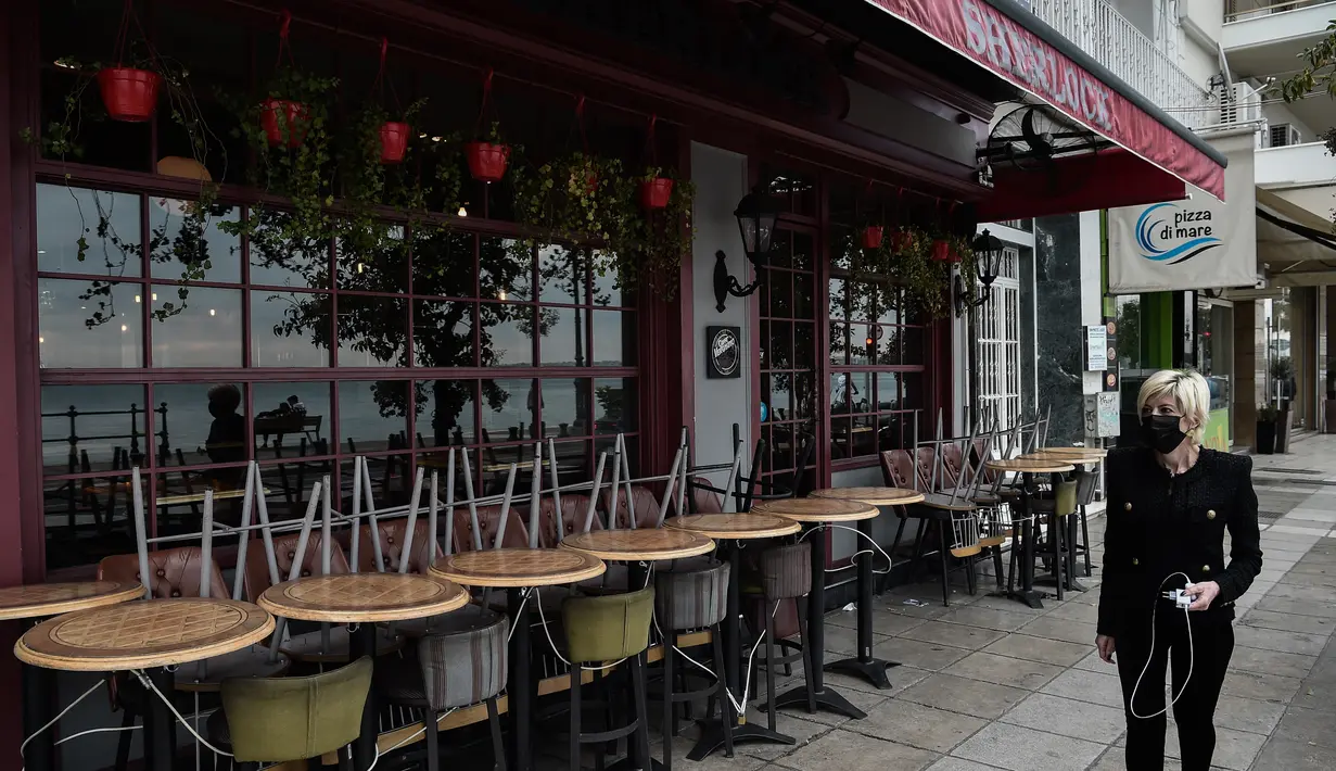 Seorang perempuan berjalan melewati kafe yang tutup di Thessaloniki, Yunani, Selasa (16/11/2021). Pemilik restoran, kafe, dan bar melakukan pemogokan selama 24 jam, memprotes aturan terkait Covid-19 dan biaya energi yang tinggi. (Sakis MITROLIDIS / AFP)