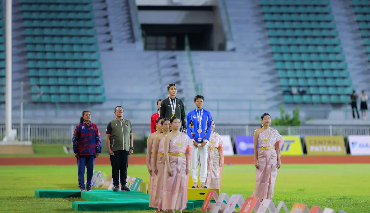 Raihan ini setelah Emilia Nova berhasil mengumpulkan total 5.497 poin sekaligus mengakhiri penantian panjangnya di nomor tersebut. Tampak dalam foto, atlet atletik Indonesia, Emilia Nova (tengah) saat prosesi penghormatan bendera usai memenangi lomba dan meraih emas nomor heptathlon (tujuh lomba) SEA Games 2025 di Stadion Supachalasai Bangkok, Thailand Selasa (16/12/2025) malam. (Bola.com/Bagaskara Lazuardi)