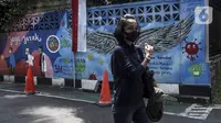 Warga yang mengenakan masker berjalan melintasi mural berisi imbauan terkait COVID-19 di Menteng, Jakarta, Kamis (7/10/2021). Menteri Kesehatan Budi Gunadi mengatakan perihal pandemi menjadi endemi dengan menyebutkan empat langkah yang dipersiapkan. (Liputan6.com/Johan Tallo)