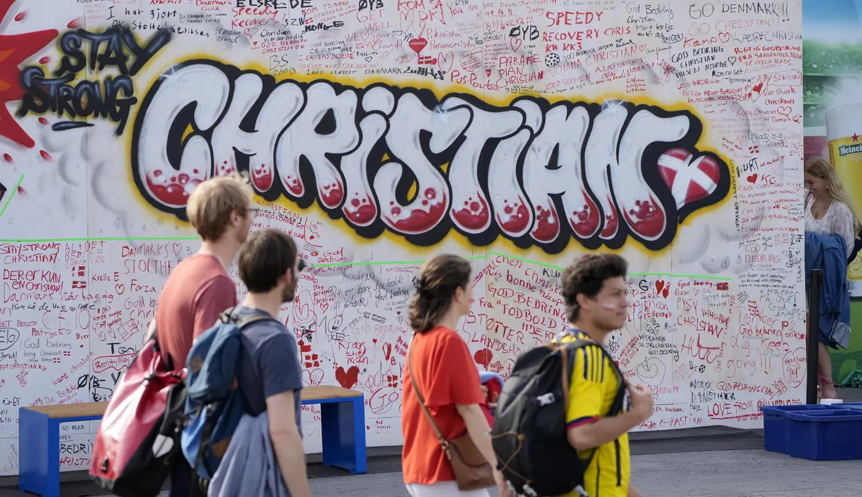 Pejalan kaki melintasi mural berisi harapan untuk gelandang timnas Denmark Christian Eriksen di dinding fanzone di Kopenhagen, Senin (14/6/2021). Eriksen mengalami serangan jantung dan sempat tak sadarkan diri saat memperkuat timnas Denmark vs Finlandia di Euro 2020. (AP Photo/Martin Meissner)