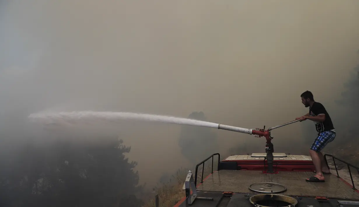 Seorang pria menyemprotkan water canon untuk memadamkan kebakaran hutan, di desa Qobayat, di utara provinsi Akkar, Lebanon, Kamis (29/7/2021). Kebakaran yang terjadi di Lebanon utara telah menghancurkan hutan pinus dan banyak desa di wilayah tersebut. (AP Photo/Hussein Malla)