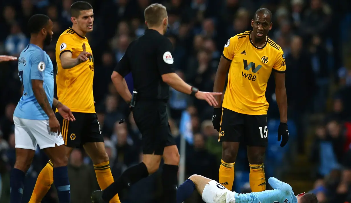 Wasit menghampiri pemain Wolverhampton Wanderers, Willy Boly (kanan) usai melanggar Bernardo Silva dalam pekan ke-22 Premier League di Stadion Etihad, Manchester, Senin (14/1). (AP Photo/Dave Thompson)