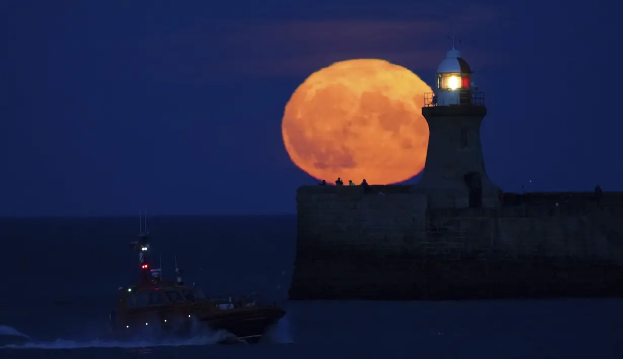 Bulan purnama yang dikenal sebagai Harvest moon muncul di atas mercusuar South Shields di pantai timur laut Inggris, Senin (20/9/2021). Ahli bulan NASA, Gordon Johnston, menerangkan harvest moon adalah bulan purnama yang paling dekat dengan titik balik musim gugur. (Owen Humphreys/PA via AP)
