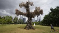 Seorang pria berjalan dengan anjingnya melewati instalasi seni karya seniman Brasil Eduardo Srur yang menggambarkan sebuah pohon terbuat dari ratusan sangkar burung sitaan polisi lingkungan dari pedagang hewan di Taman Parque do Povo, Sao Paulo, Brasil, 6 Mei 2022. Menurut Eduardo Srur, pameran "Vida Livre" atau "Kehidupan Bebas" bertujuan memprovokasi masyarakat agar memikirkan kembali budaya hewan yang terperangkap untuk hiburan manusia. (AP Photo/Andre Penner)