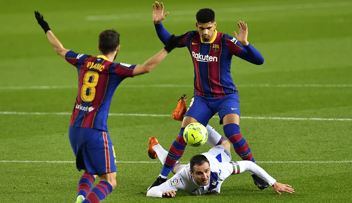 Striker Eibar, Kike Garcia (bawah) terjatuh usai perebutan bola dengan bek Barcelona, Ronald Araujo (kanan) dalam laga lanjutan Liga Spanyol 2020/21 pekan ke-16 di Camp Nou, Selasa (29/12/2020). Eibar bermain imbang 1-1 dengan Barcelona. (AFP/Pau Barrena)