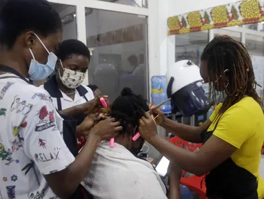 Penata rambut, memakai masker menata rambut pelanggan di dalam salon di Lagos, Nigeria, Rabu (26/5/2021). Salon tersebut menerapkan protokol kesehatan untuk para penata rambutnya saat melayani pelanggan untuk menghindari penyebaran virus Covid-19. (AP Photo/Sunday Alamba)