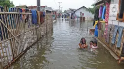 Anak-anak bermain banjir rob yang menggenangi rumah dan tambak warga di Desa Pantai Mekar, Muaragembong, Kabupaten Bekasi, Jawa Barat, Senin (6/12/2021). Banjir rob telah menggenangi wilayah tersebut selama empat hari akibat kenaikan permukaan air laut. (Liputan6.com/Herman Zakharia)