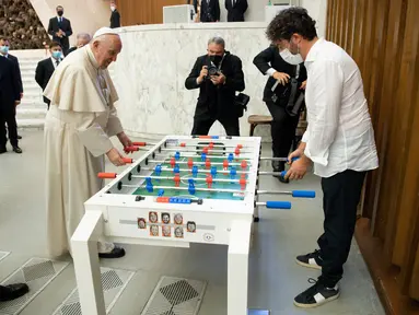 Paus Fransiskus bermain foosball atau sepak bola meja dengan Natale Tonini, presiden asosiasi Sport Toscana Calcio Balilla, pada akhir audiensi umum mingguan di Vatikan, Rabu (18/8/2021). Paus Fransiskus memang dikenal hobi bermain dan menonton sepak bola. (Vatican Media via AP)