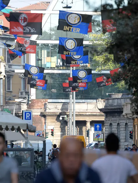 Warga melintas di bawah bendera klub Inter Milan dan AC Milan yang tergantung di jalan Paolo Sarpi, sebuah lingkungan China di Milan, Italia (13/10). Saat ini kedua tim tersebut merupakan milik pengusaha asal China. (AFP Photo/Miguel Medina)