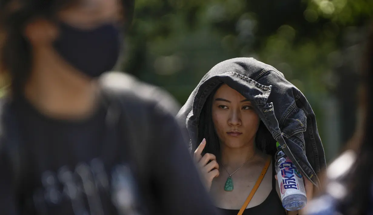 Seorang wanita menggunakan jaketnya untuk melindungi dari sinar matahari berjalan di sepanjang jalan saat ibu kota dilanda gelombang panas di Beijing, Senin, 5 Juni 2023. (AP Photo/Andy Wong)