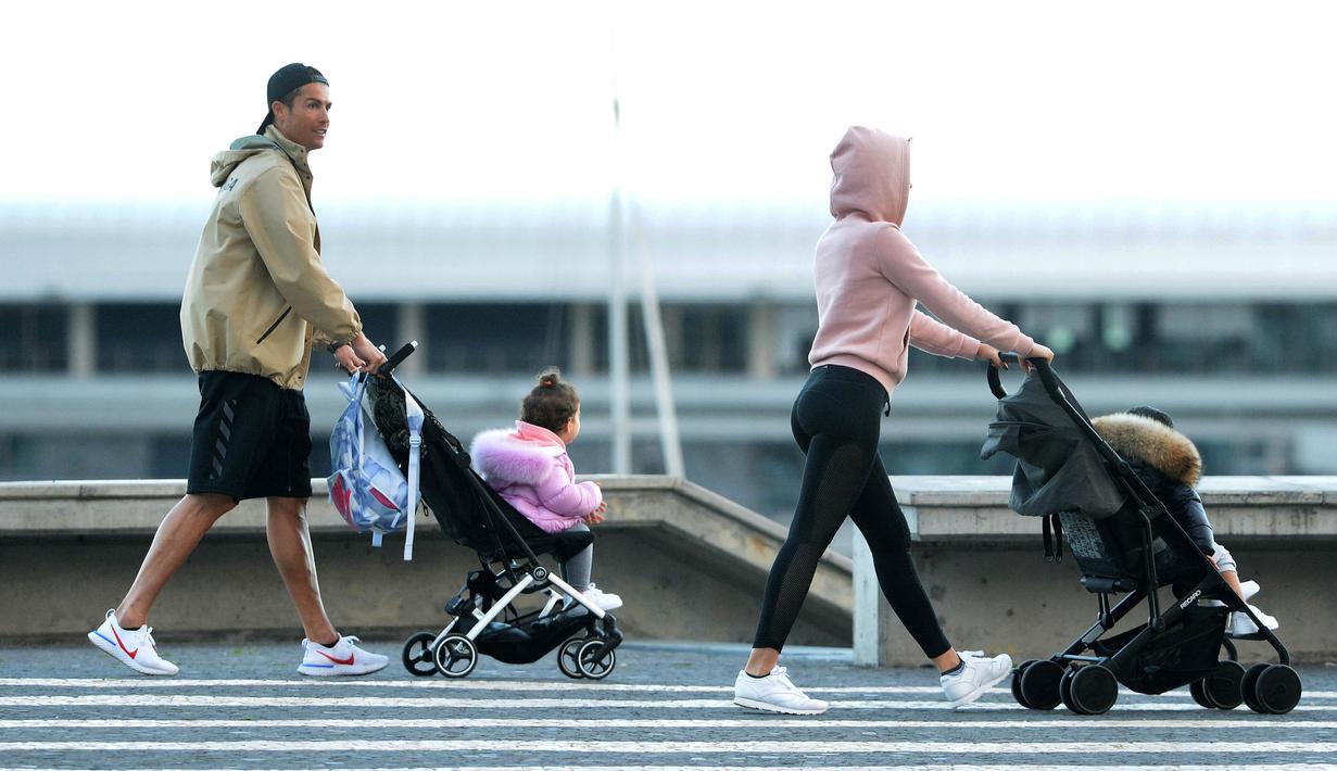 Cristiano Ronaldo bersama kekasihnya Georgina Rodriguez mengajak anak-anaknya berjalan santai di Funchal, Portugal, Sabtu (28/3/2020). Bintang Juventus ini memilih pulang kampung saat Serie A dihentikan sementara karena wabah virus corona. (AFP/Helder Santos)