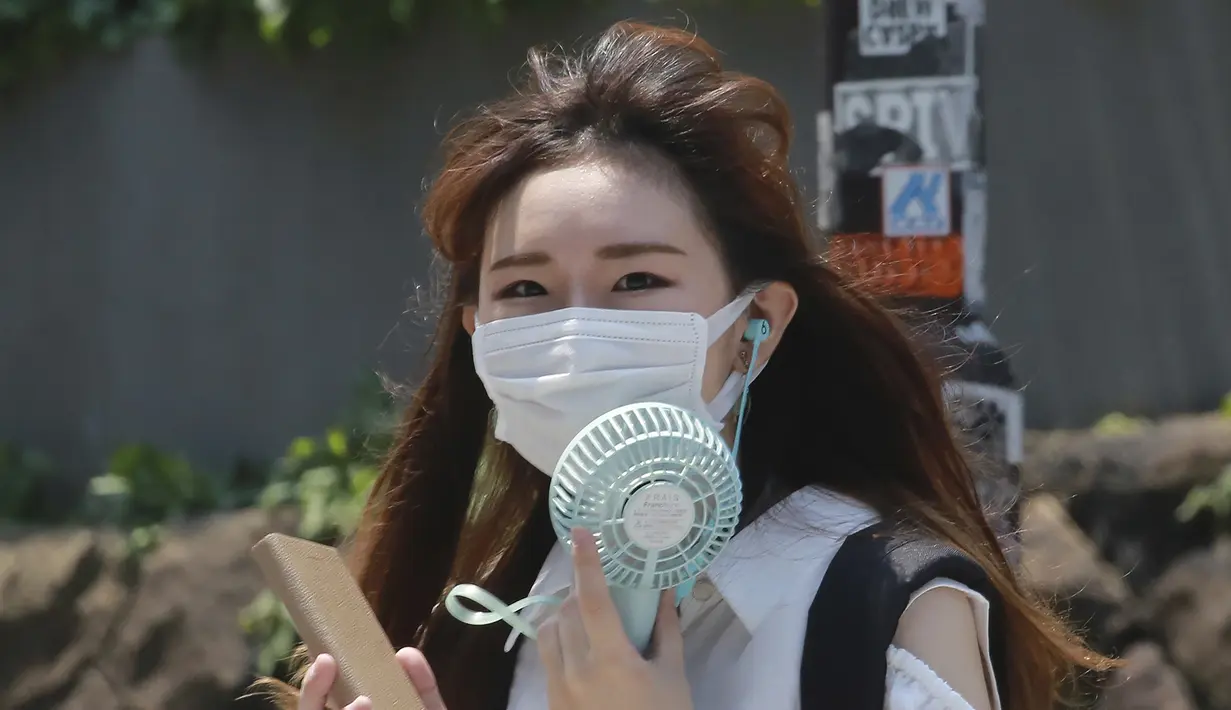 Seorang wanita mengenakan masker untuk membantu melindungi dari penyebaran coronavirus memegang kipas angin portabel untuk menghindari panas di Tokyo, Rabu, (5/8/2020). (AP Photo/Koji Sasahara)