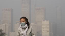 Seorang wanita mengenakan masker untuk melindungi diri dari COVID-19 berjalan di depan gedung perkantoran di Kawasan Pusat Bisnis yang diselimuti kabut polusi di Beijing, Kamis (18/11/2021).  (AP Photo/Andy Wong)