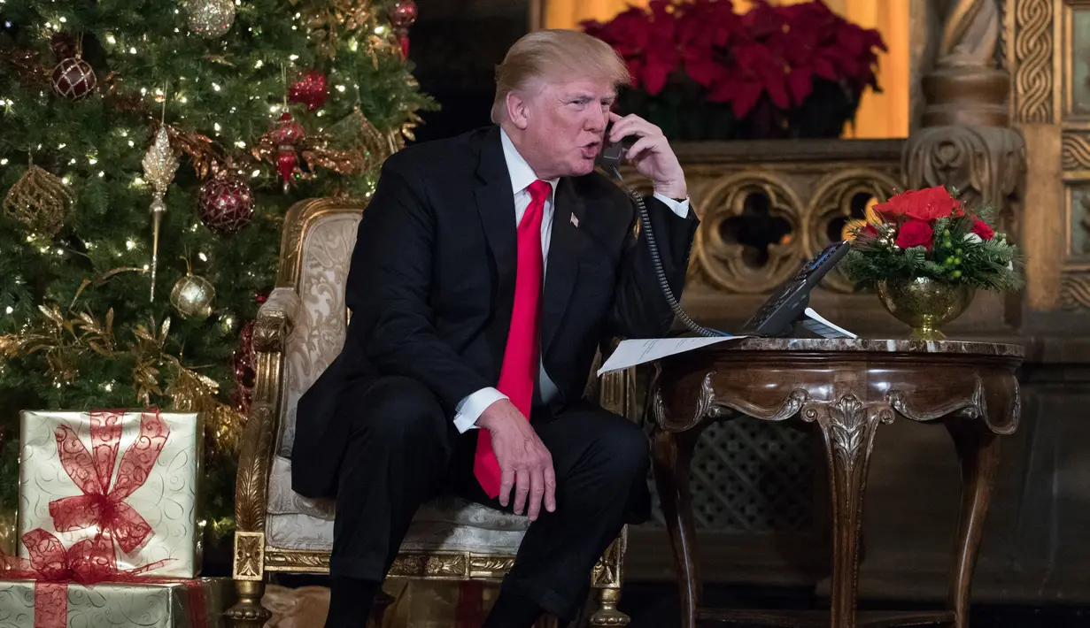 Presiden Donald Trump berbicara dengan anak-anak di telepon saat mereka mengiktui NORAD Tracks Santa di Palm Beach, AS (24/12). Acara NORAD Tracks Santa ini mengandalkan sukarelawan untuk menerima telepon dari anak-anak. (AP Photo/Carolyn Kaster)