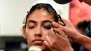 Seorang model India saat dirias oleh kru makeup di belakang panggung sebelum tampil di catwalk selama Lakmé Fashion Week (LFW) Summer Resort 2019 di Mumbai, India (31/1). (AFP Photo/Sujit Jaiswal)